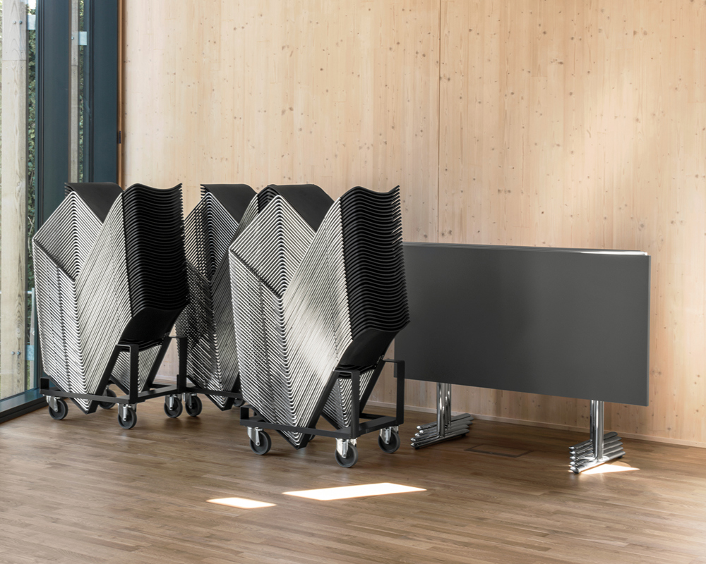 A group of stacked 40/4 black chairs on dollies and flipped Tempest tables 