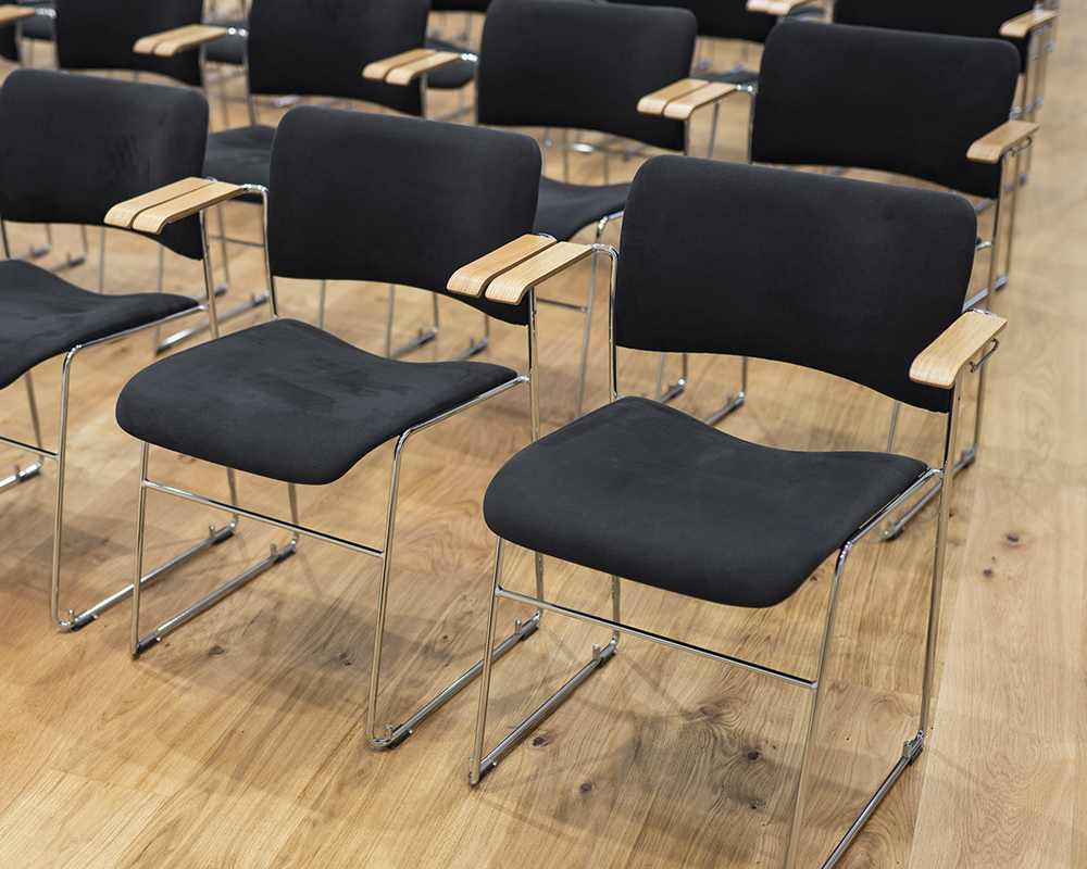 An installation of numerous black-upholstered 40/4 armchairs with a focus on the oak veneer armrests with arm linking