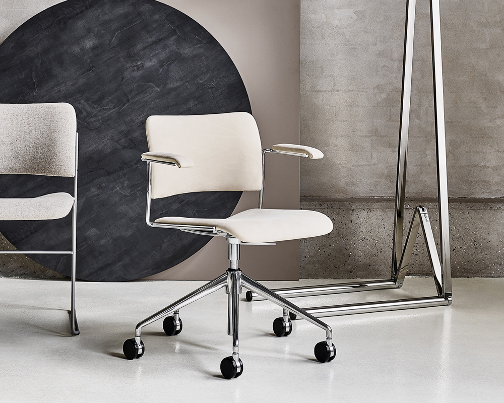 An installation with a white leather-upholstered 40/4 swivel armchair in front, 40/4 side chair in the back, and two table tops and Simpla frame against a concrete wall