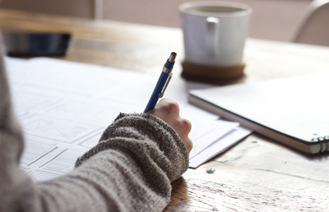 A closeup image of a hand with a pen over papers 