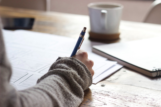 A closeup image of a hand with a pen over papers