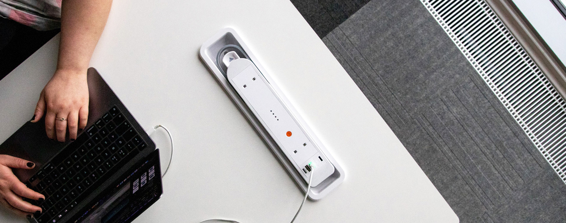 A close-up image of a person working on a laptop at a table with a white built-in battery in the tabletop