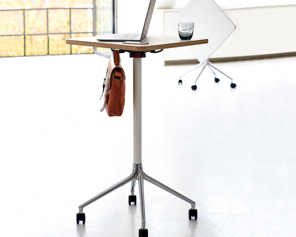An installation of two white, square AS500 tables in an empty room with big windows. The one in front has work attributes, and the one in back is flipped